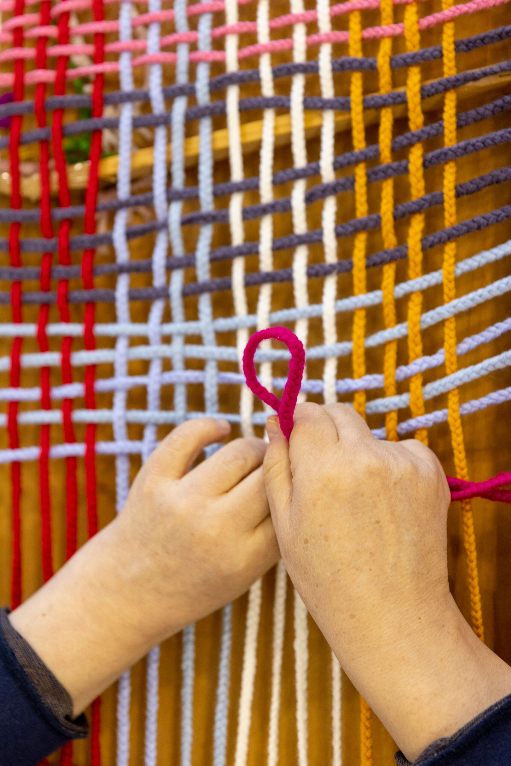 Delle mani intrecciano fili di lana colorati su un telaio